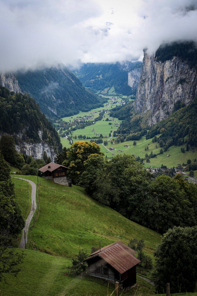 Breathtaking view of a lush alpine valley with tall cliffs, huts, and greenery.
