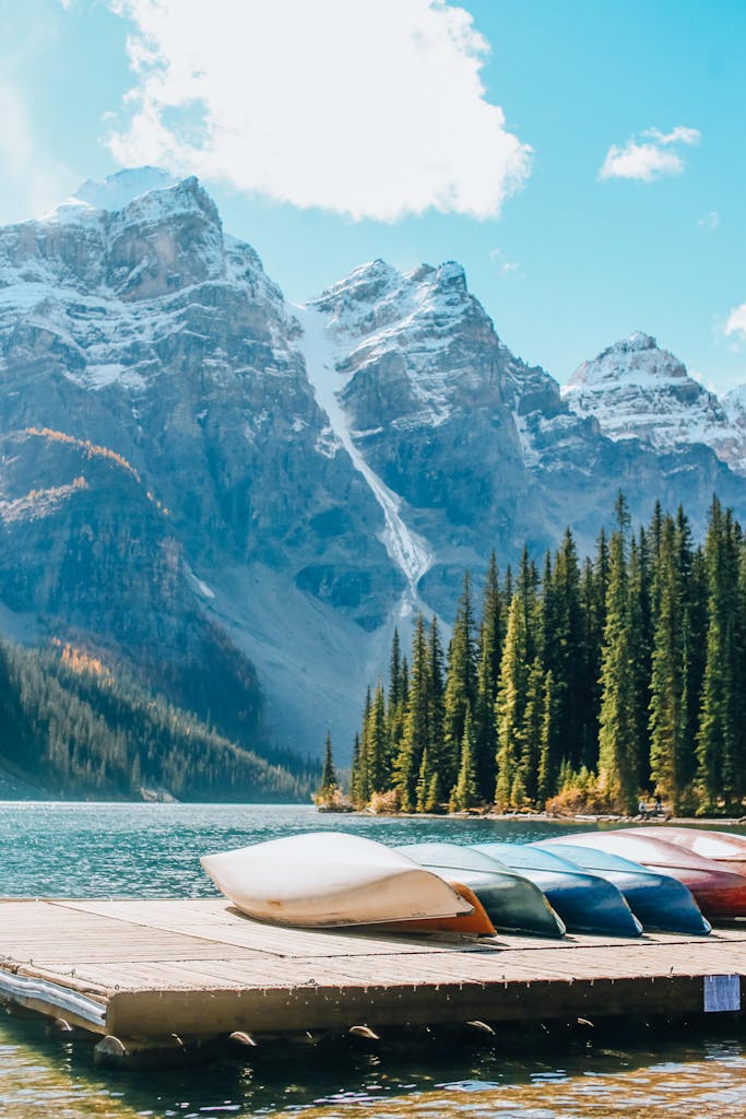 Canoes on a wooden dock by Lake Moraine, surrounded by majestic mountains and a forest under a bright blue sky.