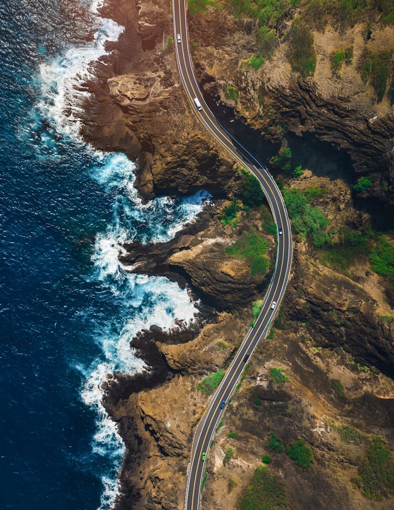Stunning aerial shot of a winding coastal road in Hawaii with vibrant ocean waves.