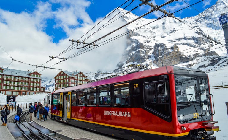 From below of contemporary train on railway near group of anonymous travelers on platform behind snowy mountain and buildings in winter