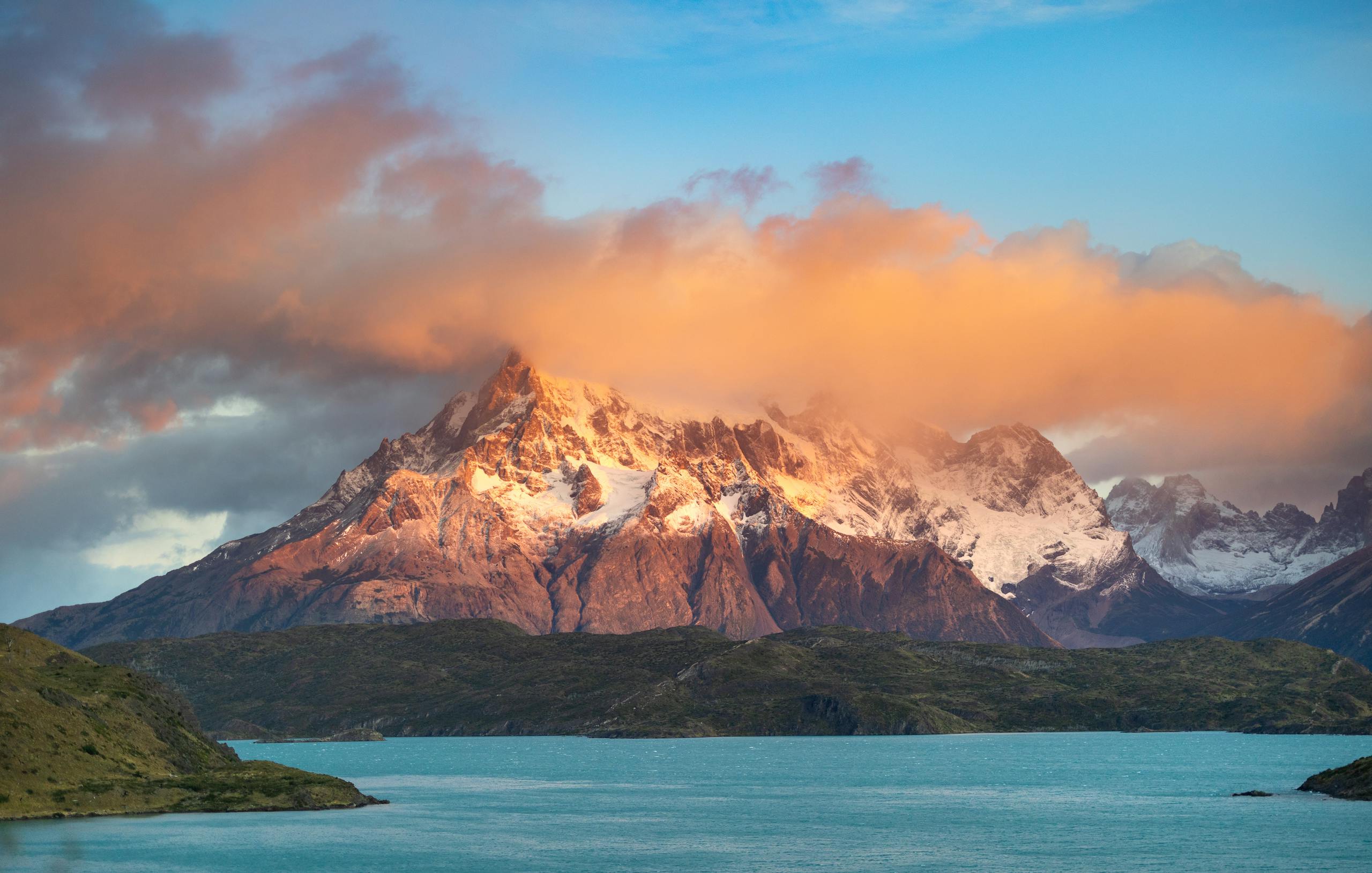 Epic sunrise view of snow-capped Torres del Paine mountains in Chile with colorful clouds.
