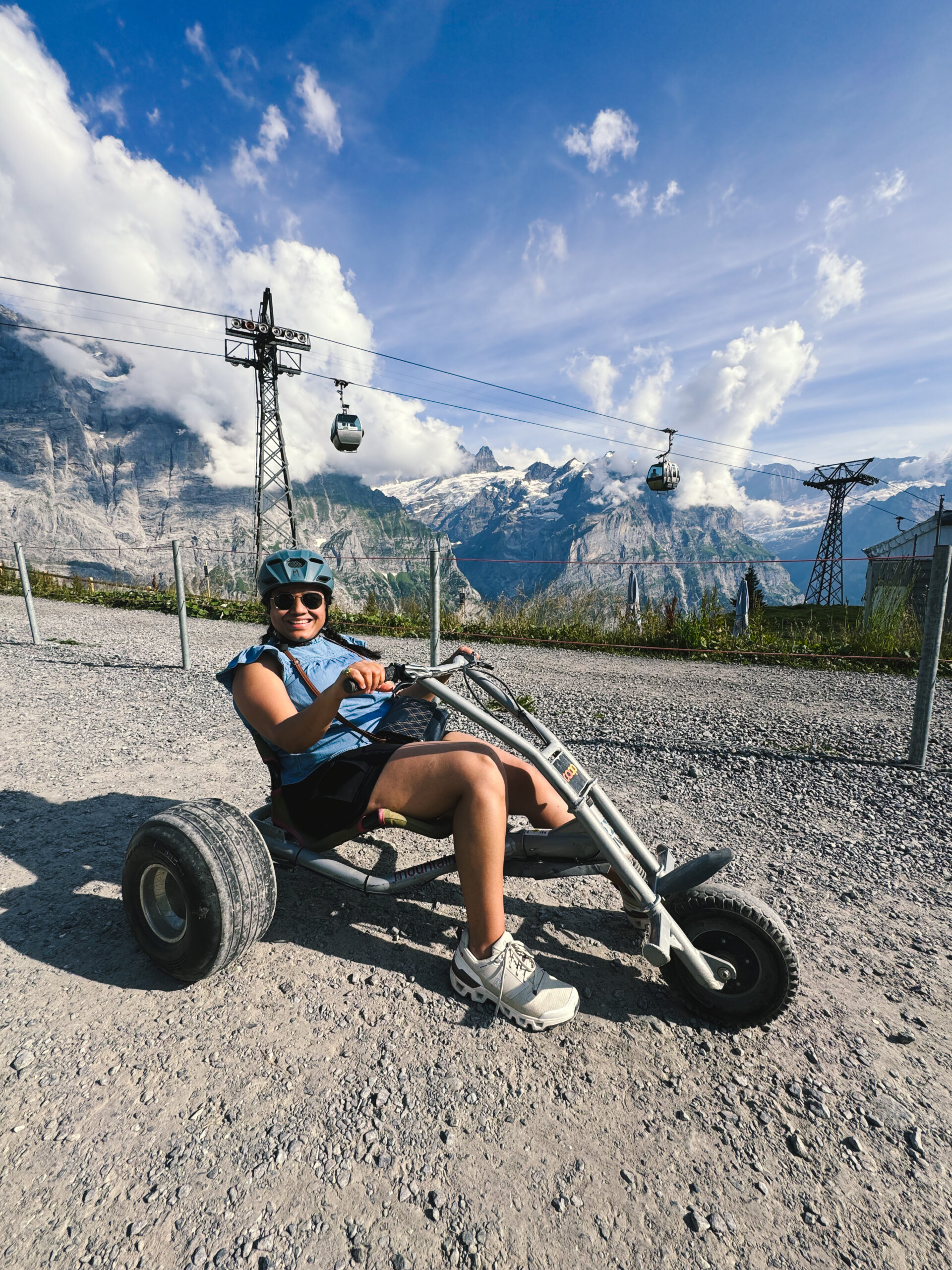 Riding a mountain cart down the gravel track at Grindelwald First, gondola cables and snowy peaks behind